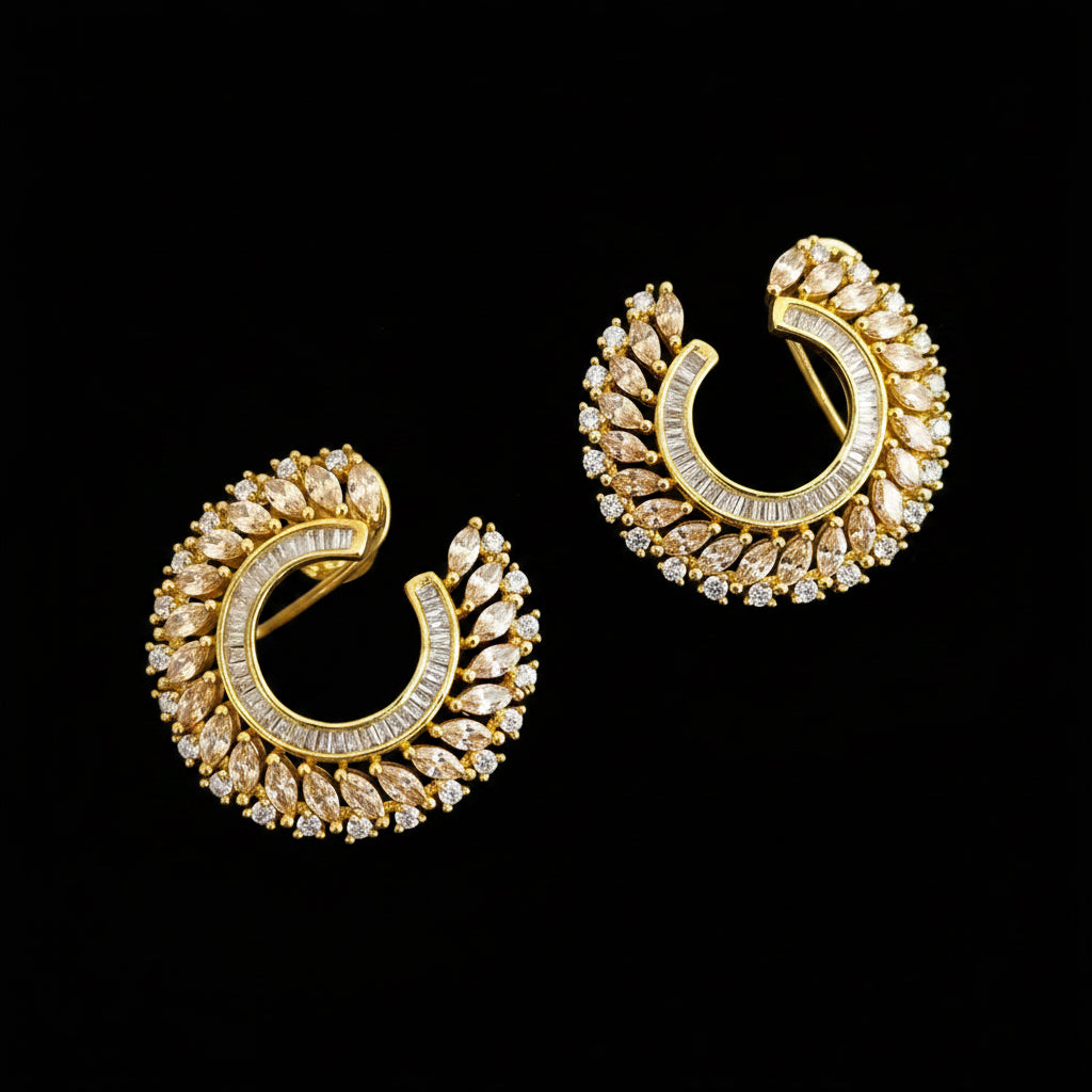A pair of gold crescent-shaped hoop earrings adorned with clear pavé stones, displayed on a dark reflective surface with the brand logo 'SAHELL MYBESTFRIEND' visible above.