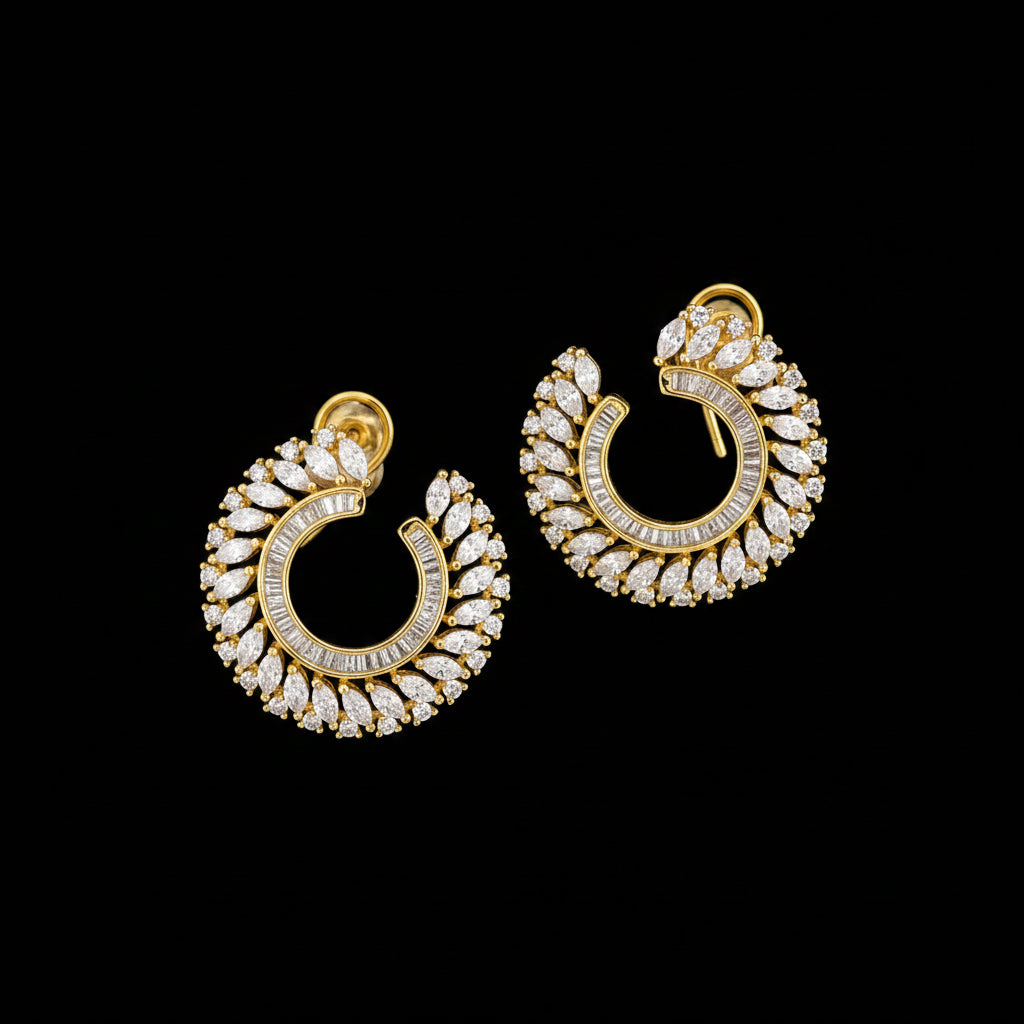 A pair of gold crescent-shaped hoop earrings adorned with clear pavé stones, displayed on a dark reflective surface with the SAHELI MY BEST FRIEND logo above.