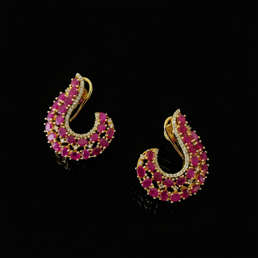 A pair of gold crescent-shaped hoop earrings embellished with rows of vibrant pink gemstones and small clear stones, displayed on a dark reflective surface with the brand logo 'SAHELI MY BEST FRIEND' in the background.