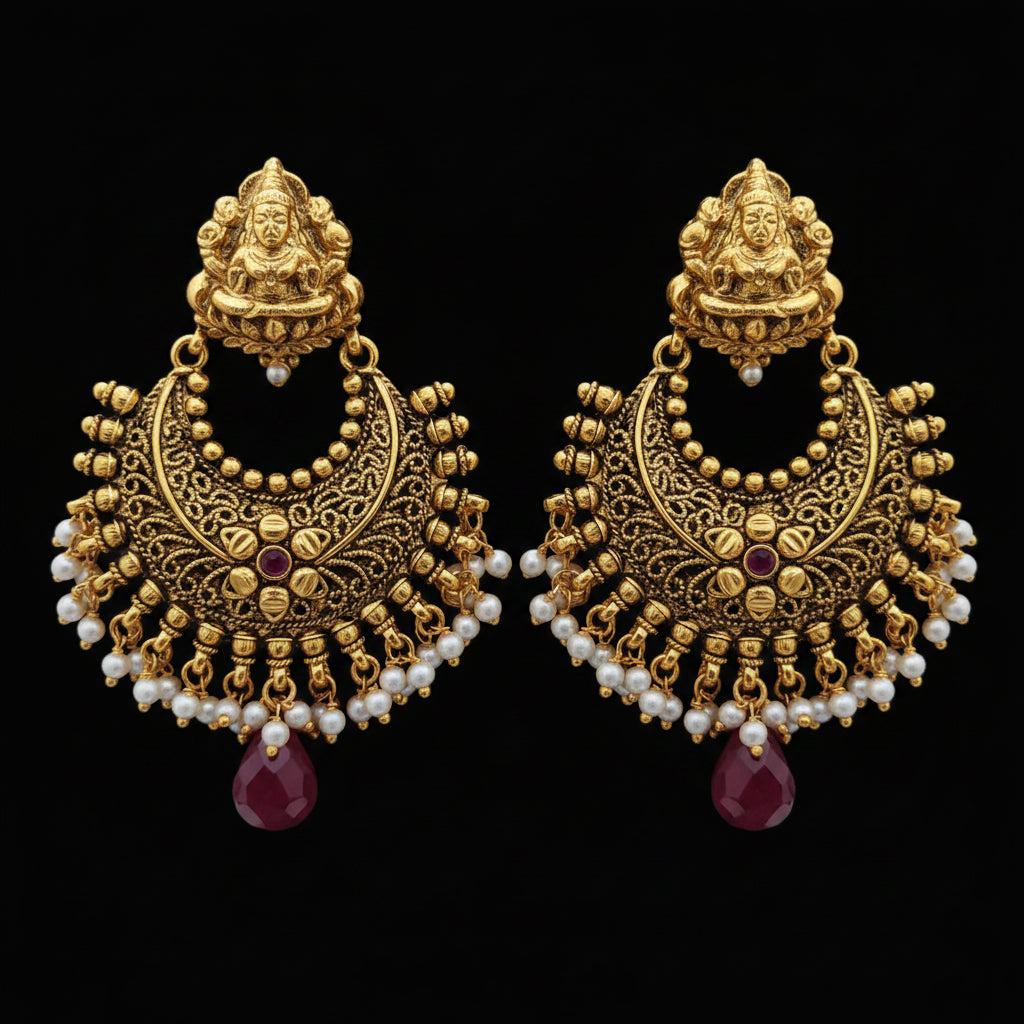 A pair of ornate gold-toned traditional Indian jhumka earrings with white pearl bead strands and red gemstone accents, displayed on a gray laptop keyboard.