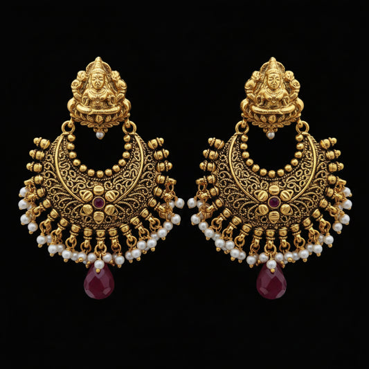 A pair of ornate gold-toned traditional Indian jhumka earrings with white pearl bead strands and red gemstone accents, displayed on a gray laptop keyboard.