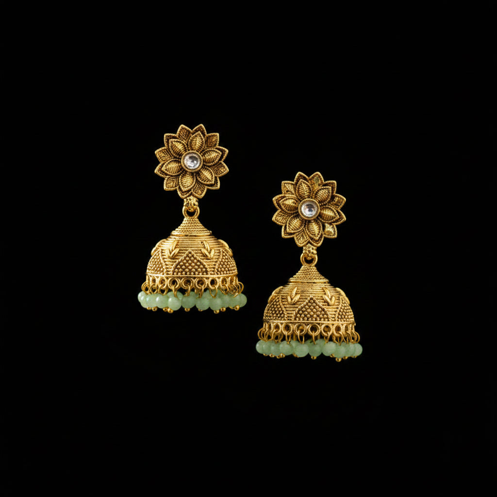 Gold floral earrings with green stones on a black stand against a dark background