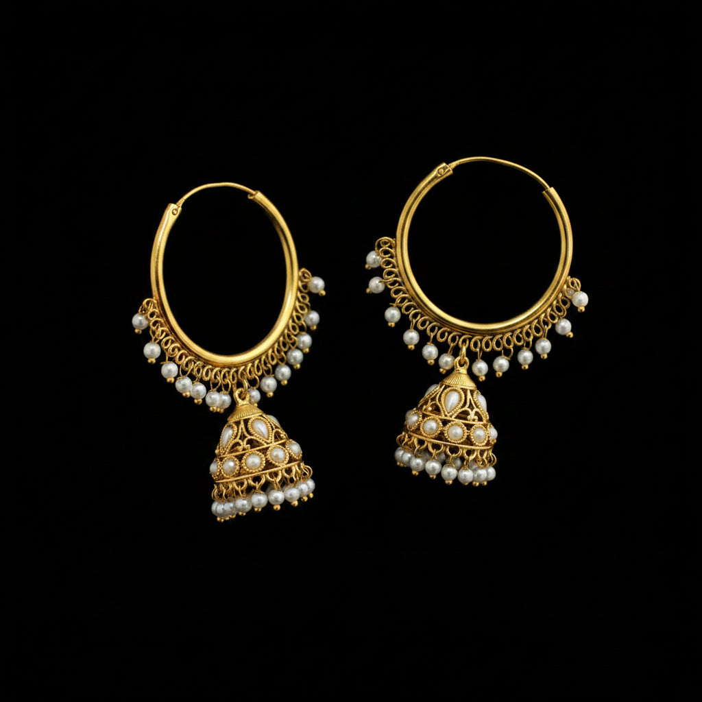A pair of gold-toned traditional hoop earrings with dangling bell-shaped jhumka motifs, decorated with white pearls, displayed on a black stand against a dark gray background.