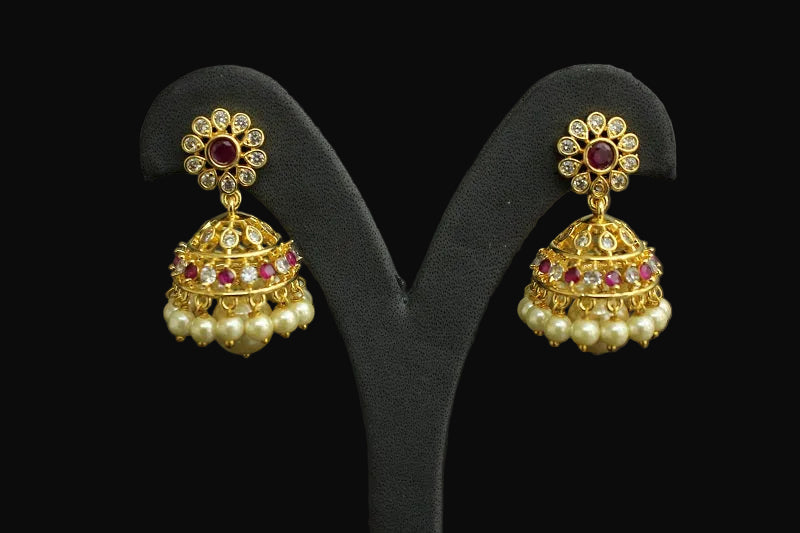 Gold earrings with pearls and red gemstones on a black stand, branded 'Saheli'.