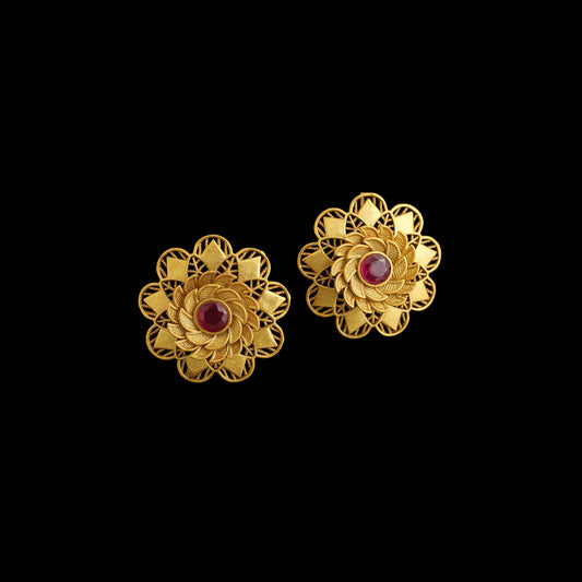 Pair of gold flower-shaped earrings with red centers on a dark background