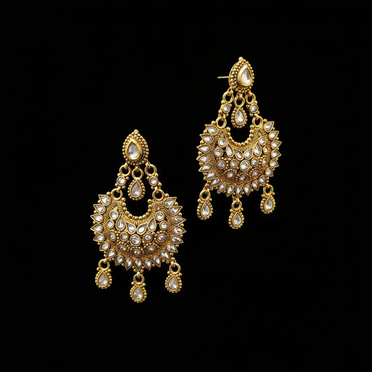 A pair of ornate gold-toned dangle earrings with clear stones, displayed on a gray stand against a gray background with the brand name SAHELI MY BEST FRIEND printed above.