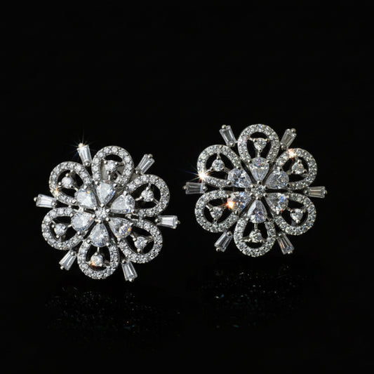 Pair of silver floral earrings on a black background with 'SAHELI' branding.
