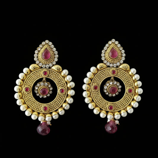 A pair of traditional Indian gold-toned chandelier earrings with white faux pearls, pink gemstone accents, and clear rhinestone detailing, displayed on a dark reflective surface with the brand name 'SAHELI MY BEST FRIEND' printed above.