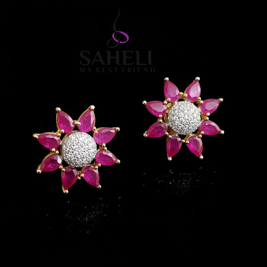 Pair of pink flower-shaped earrings with clear center on a gray background, branded 'SAHELI'.