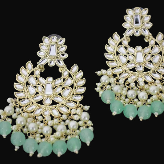 Pair of ornate earrings with green beads on a dark background