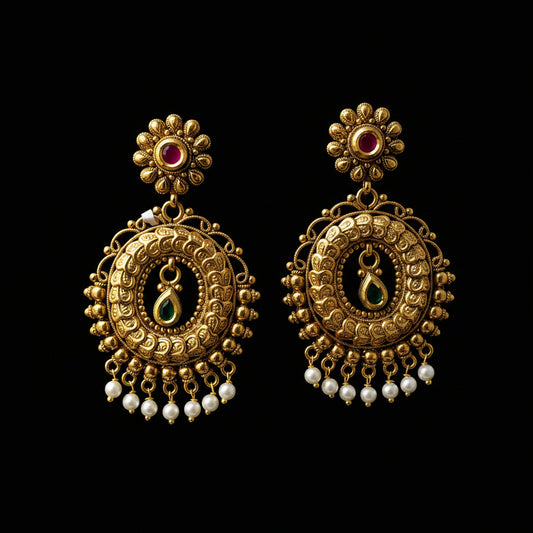 Gold earrings with red and green gemstones on a gray background, branded 'Saheli'.