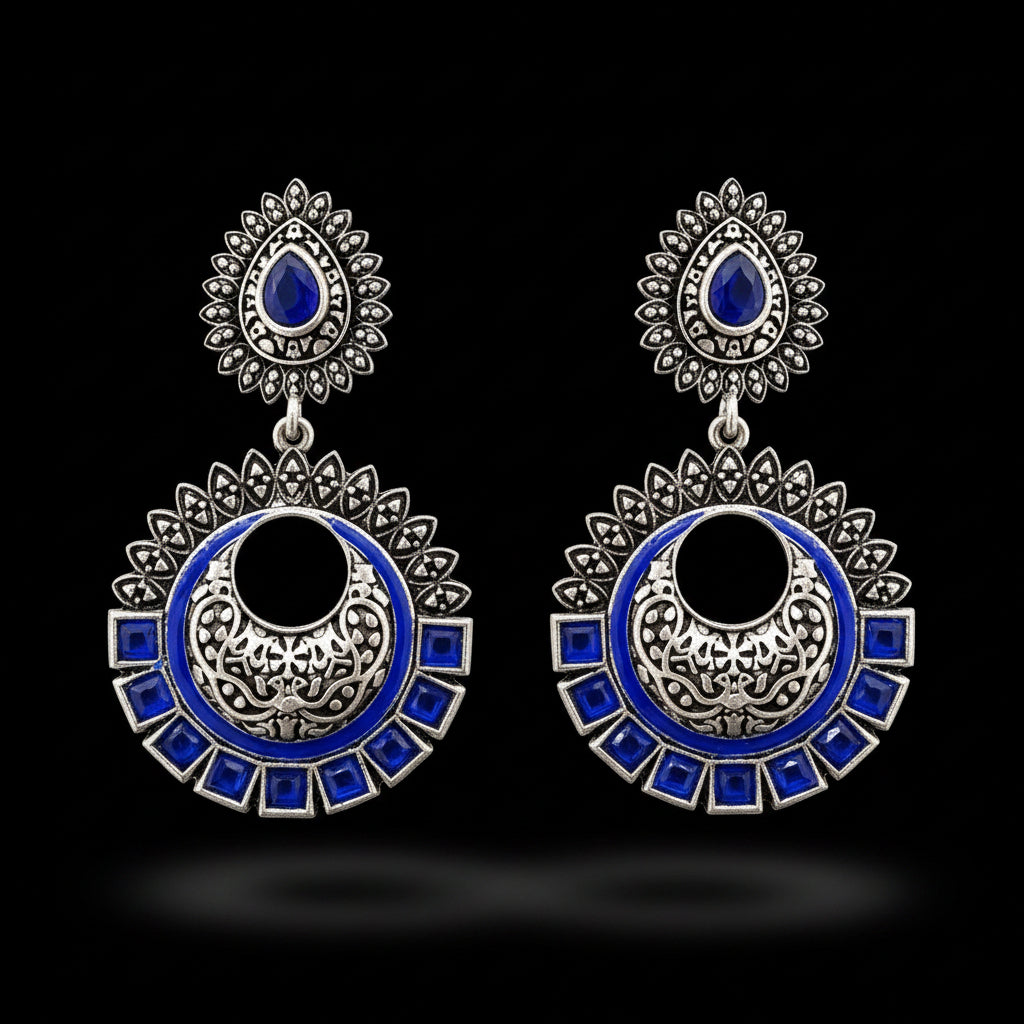 Ornate silver and blue earrings on a stand with 'SAHELI' branding.