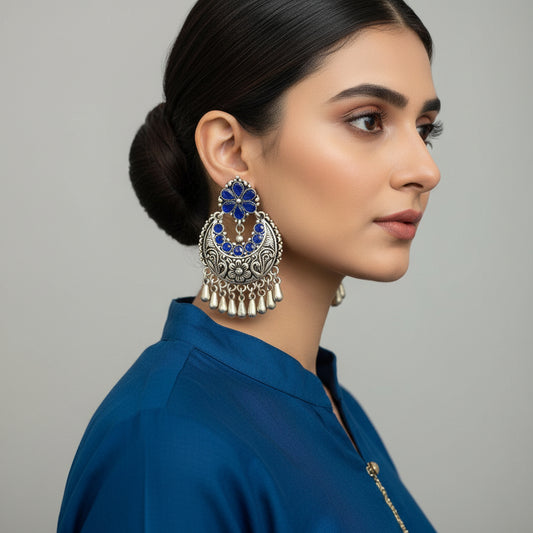 Pair of silver and blue floral earrings on a dark background with 'SAHELI' branding.