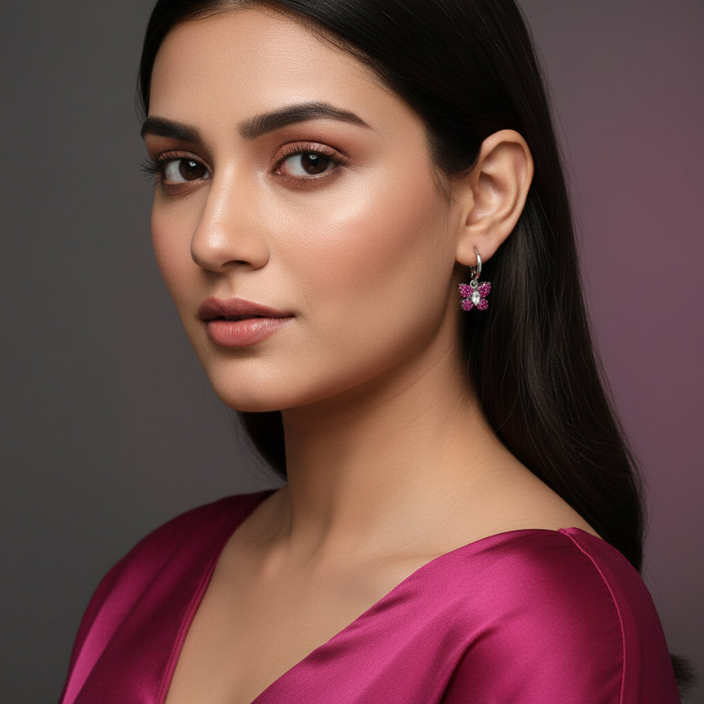 Butterfly-shaped earrings with pink gemstones on a dark background, branded 'Saheli'.