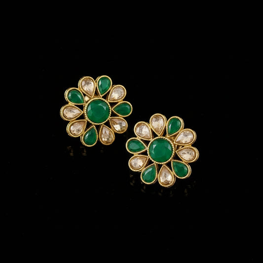 Floral earrings with green gemstones and gold accents on a gray background, featuring the brand 'Saheli'.