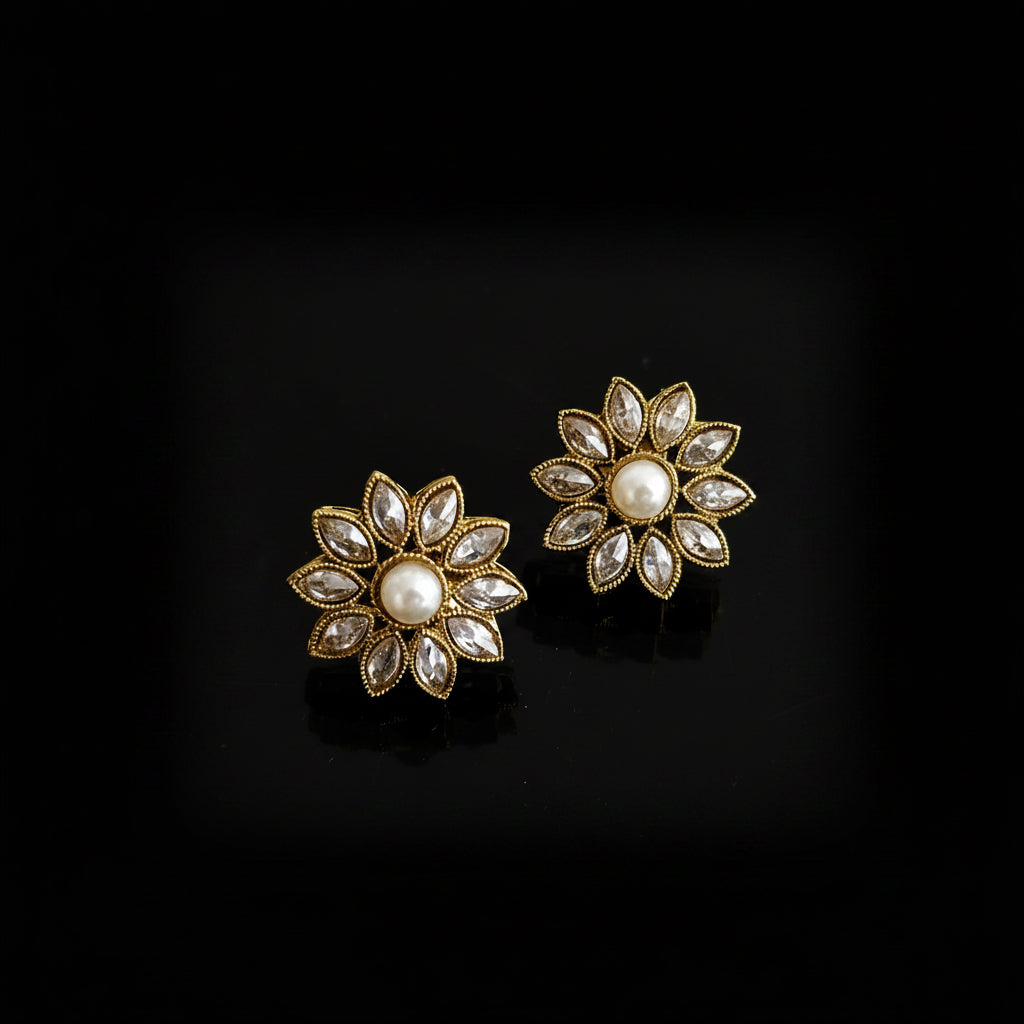 Gold floral earrings with pearl-like centers on a gray background, featuring the brand 'SAHELI'.