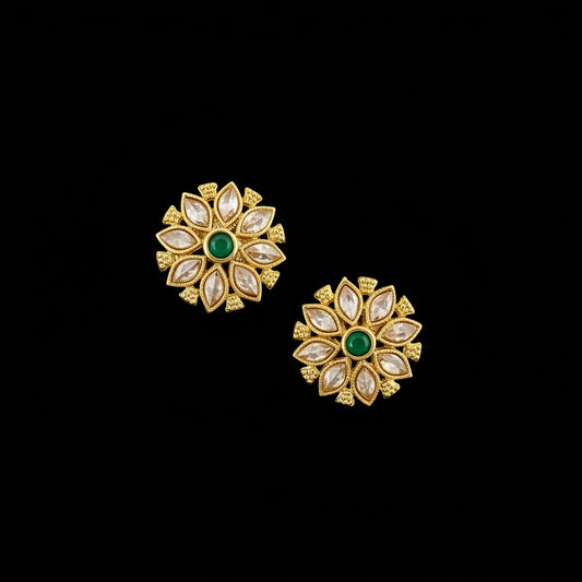 Gold floral earrings with green gemstones on a gray background, featuring the 'SAHELI' brand.