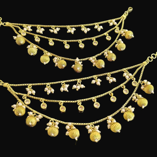 Gold necklace with pendants on a dark background, featuring the brand 'Saheli'.