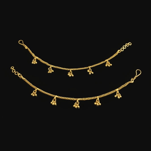 Gold anklets with dangling charms on a black background