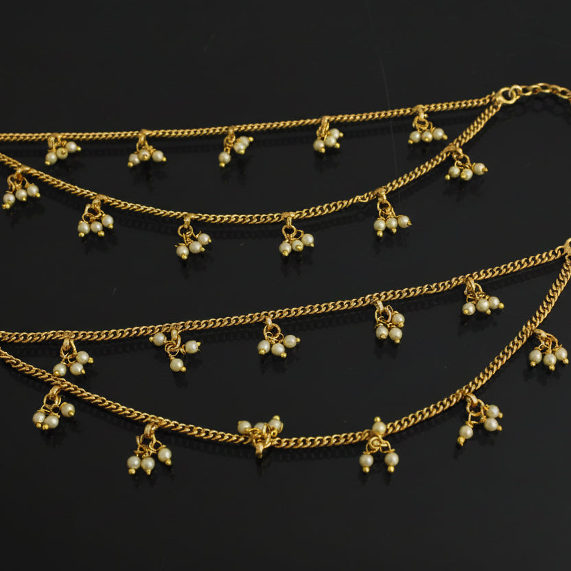 Two gold anklets with pearl-like beads on a black background