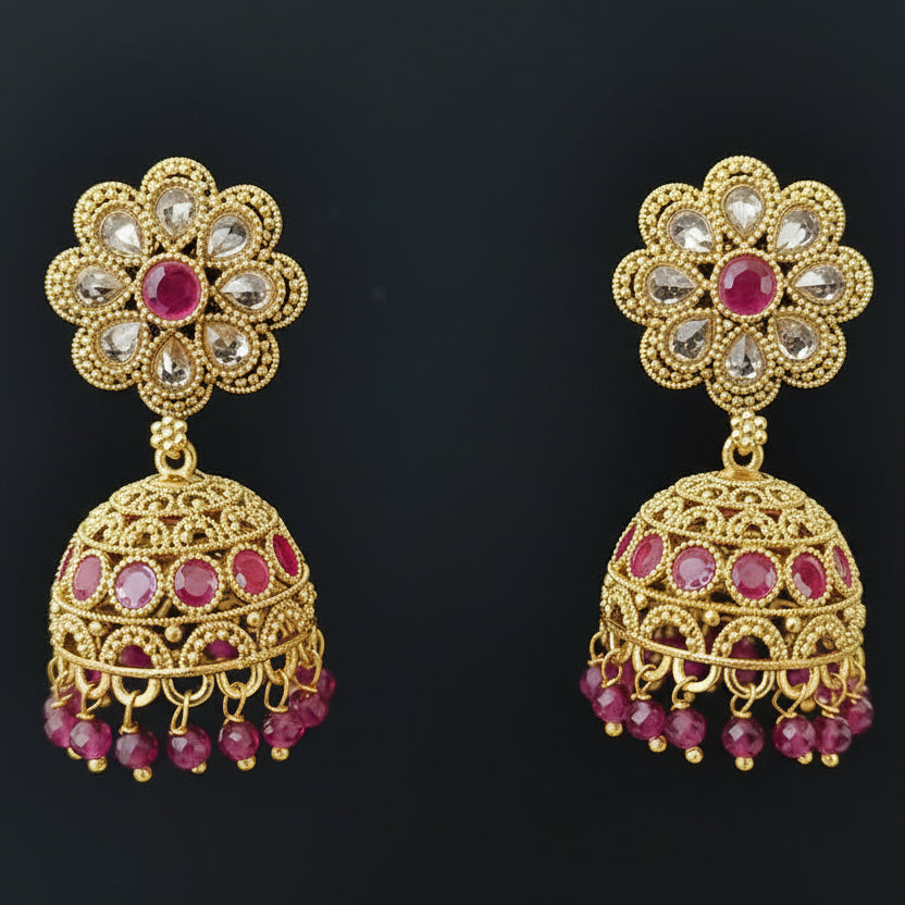 Gold and pink floral earrings on a gray stand against a black background