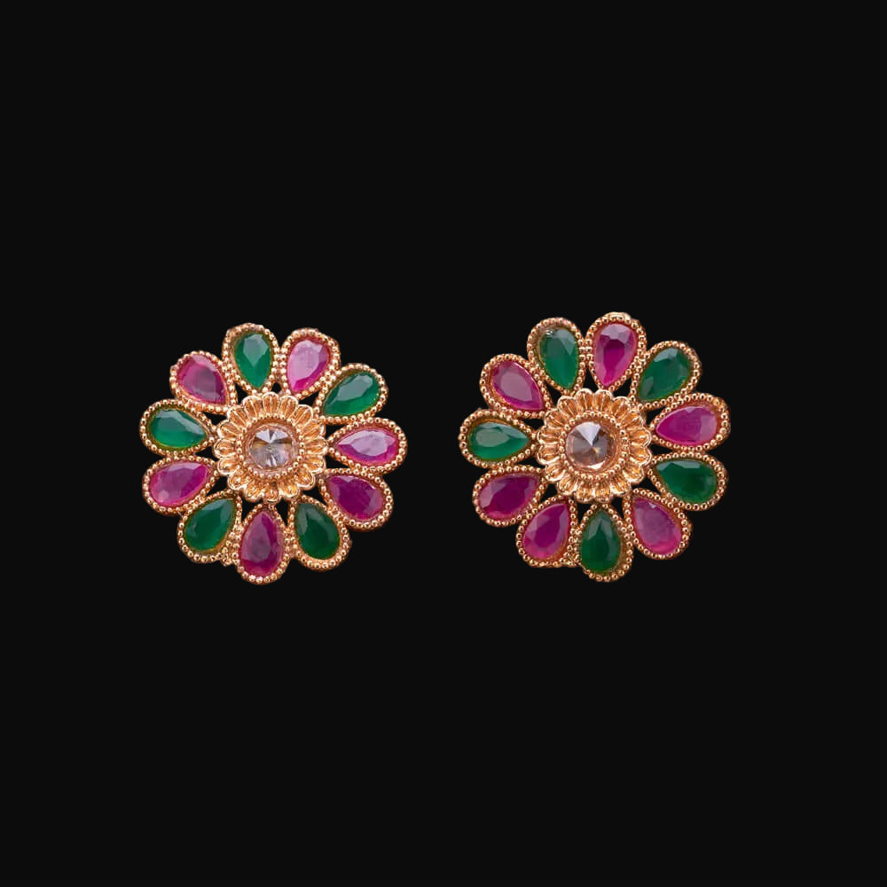 Pair of floral earrings with green and pink stones on a wooden surface