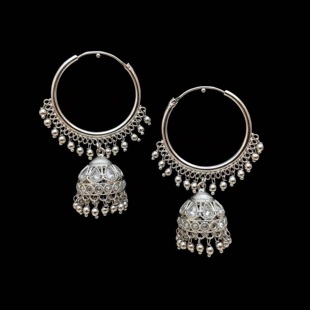 Silver hoop earrings with jhumka designs on a dark stand, branded 'Saheli'.