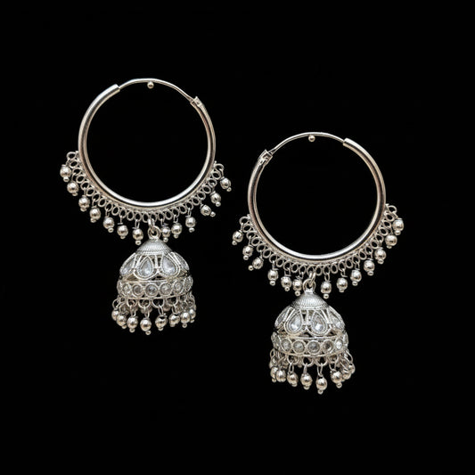 Silver hoop earrings with jhumka designs on a dark stand, branded 'Saheli'.