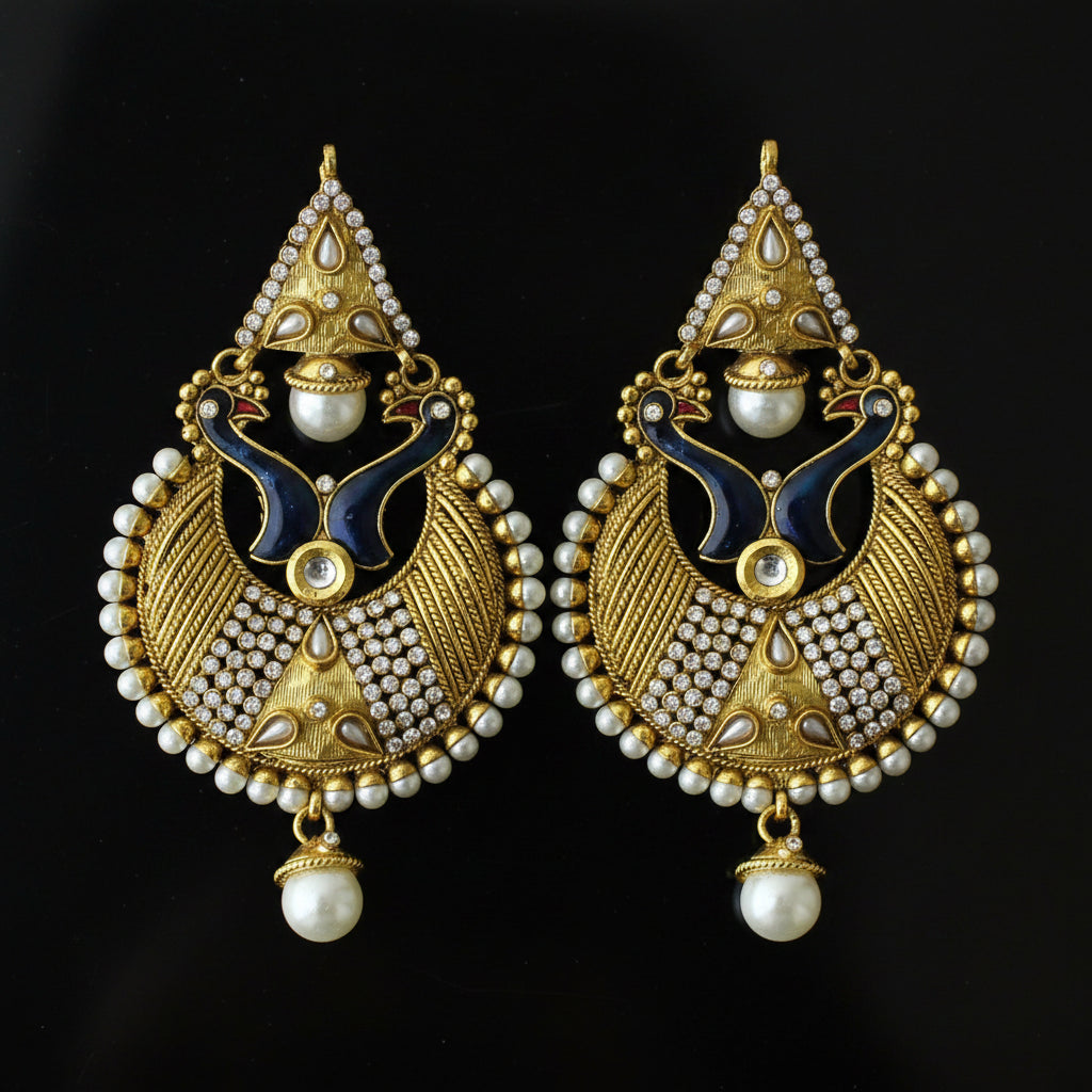 A pair of traditional Indian gold-plated earrings with intricate filigree, white faux pearls, and dark blue enamel details, displayed on a dark reflective surface. The Saheli My Best Friend logo is visible in the top left corner.