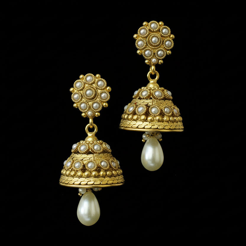 Gold and pearl earrings on a black stand with 'Saheli' branding.
