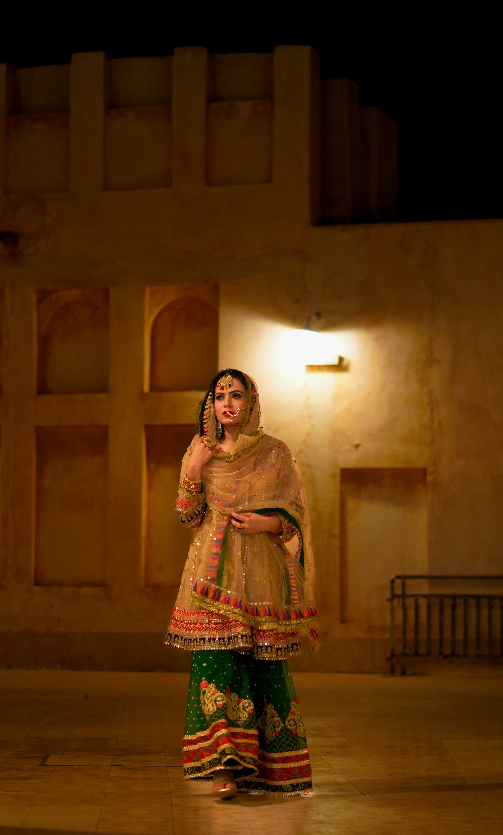 Woman in traditional attire standing in a dimly lit room with stone walls.