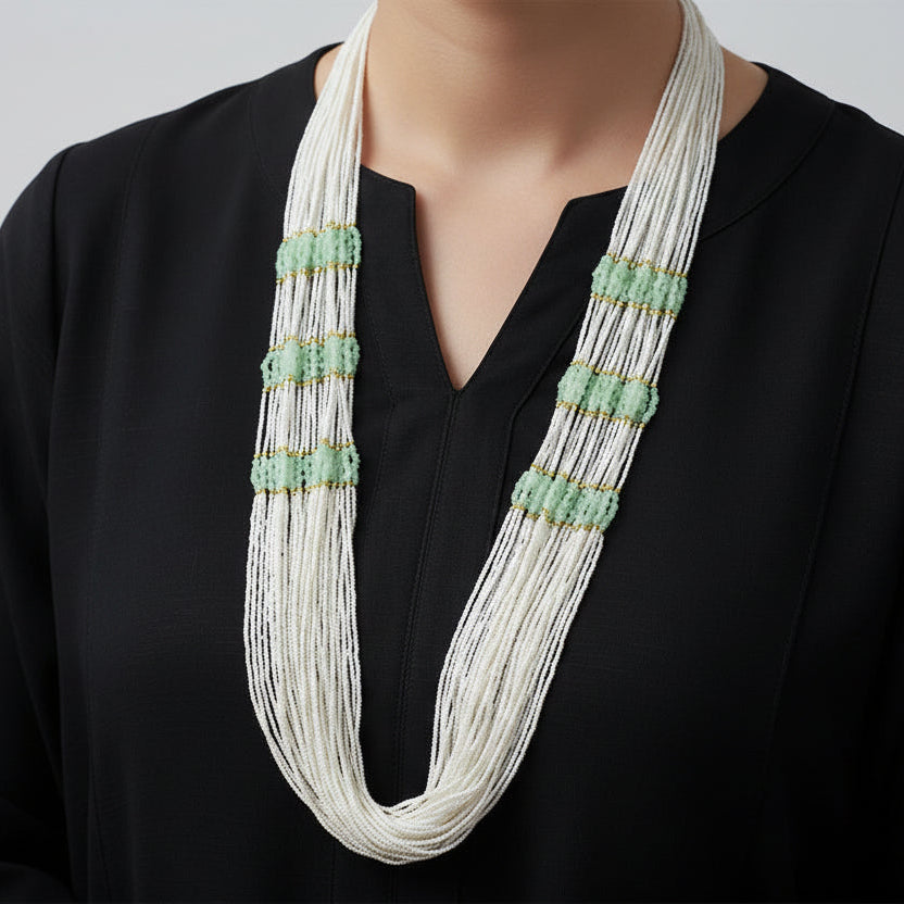 Long beaded necklace with white and green beads on a dark background
