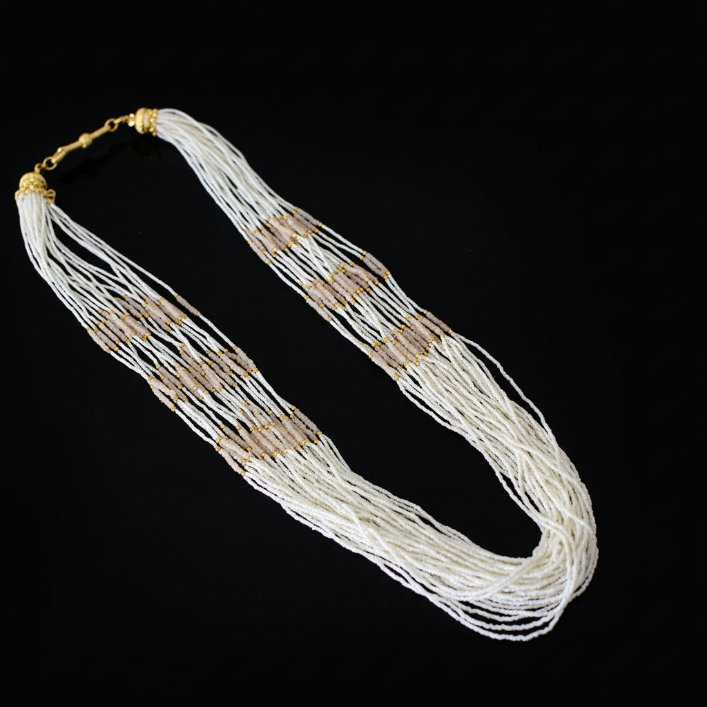 Long necklace with white and gold beads on a dark background