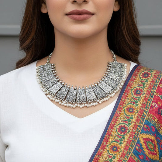 Silver necklace with intricate designs on a gray background, featuring the brand 'Saheli'.