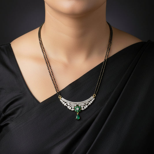 A traditional Indian Mangalsutra necklace with a black beaded chain and a gold-plated pendant decorated with white stones and a green stone, displayed on a dark reflective surface. The brand logo 'SAHELI MY BEST FRIEND' is visible in the top left.