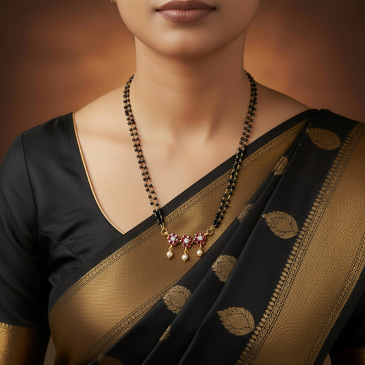 A traditional Indian black bead and gold chain necklace (manglik) featuring a central gold pendant decorated with pink gemstones and three dangling white pearl beads, shown on a dark gray background.