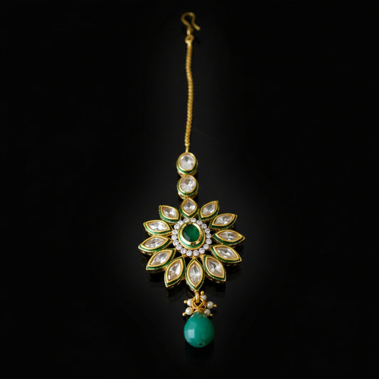 Jewelry pendant with green gemstone on a dark background, featuring the brand 'Saheli'.