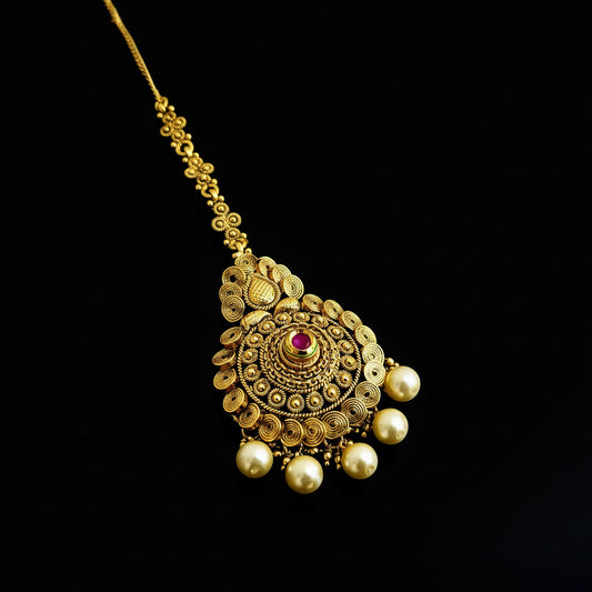 Gold necklace with pearl drops and a red gemstone on a dark background, branded 'SAHELI'.