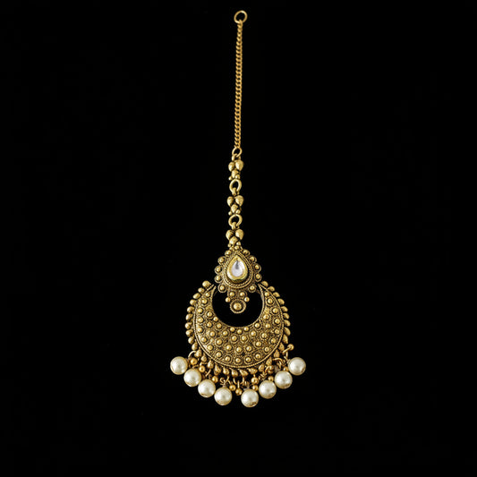 Gold necklace with pearl accents on a dark background, featuring the brand 'Saheli'.