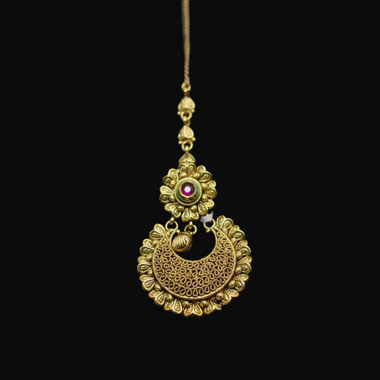 Gold necklace with a floral design and red gemstone on a dark background