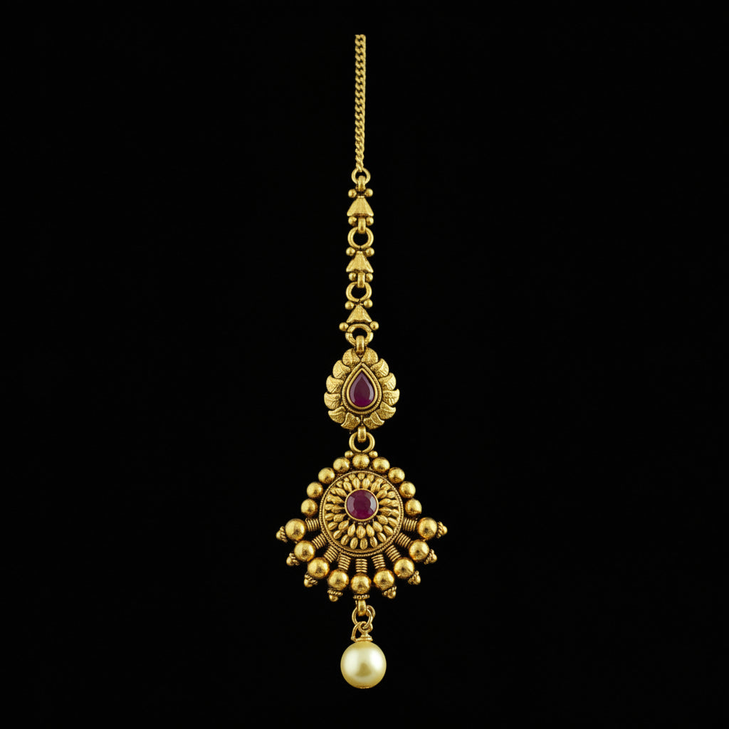 Gold necklace with red stones and a pearl on a dark background, featuring the brand 'Saheli'.