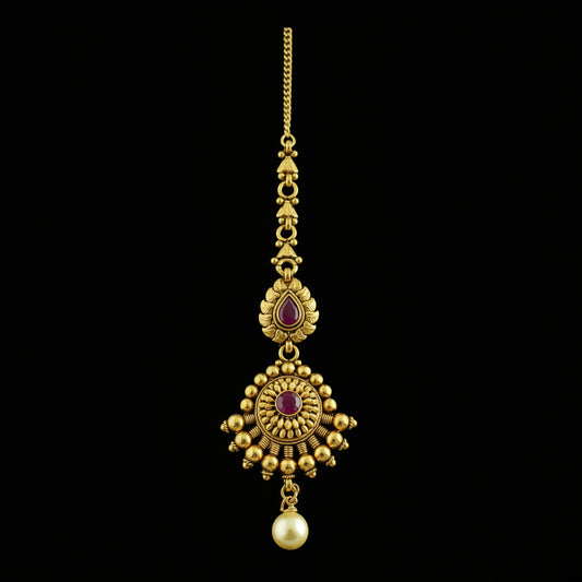 Gold necklace with red stones and a pearl on a dark background, featuring the brand 'Saheli'.