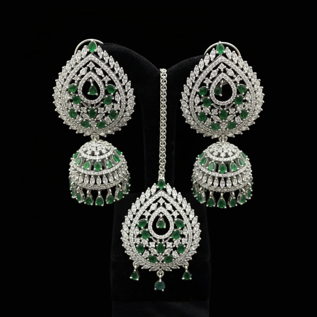 Ornate earrings with green gemstones on a black stand, featuring the brand 'Snehell'.