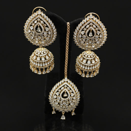 Ornate gold earrings with intricate designs on a dark stand, branded 'Saheli'.