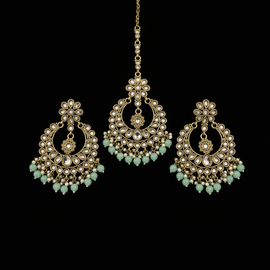Ornate gold earrings with green stones on a dark background
