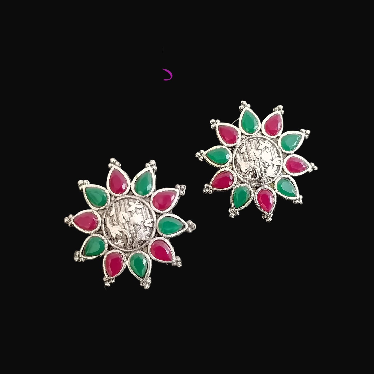Pair of silver earrings with red and green gemstones on a gray background, featuring the brand 'Saheli'.
