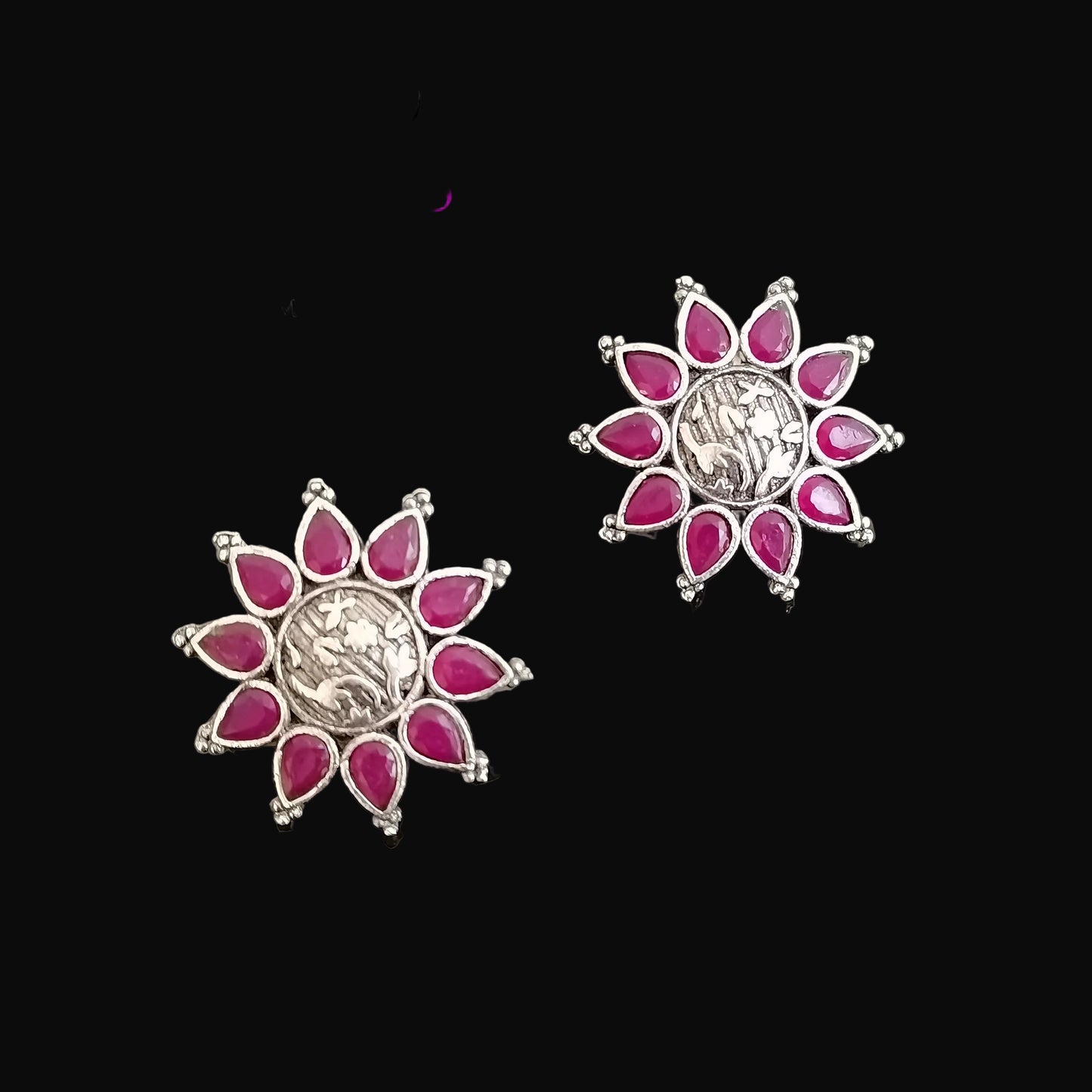 Pair of flower-shaped earrings with pink gemstones on a gray background, featuring the brand 'Saheli'.