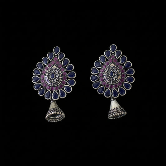 Pair of ornate earrings with purple and blue stones on a dark background, branded 'SAHELI'.