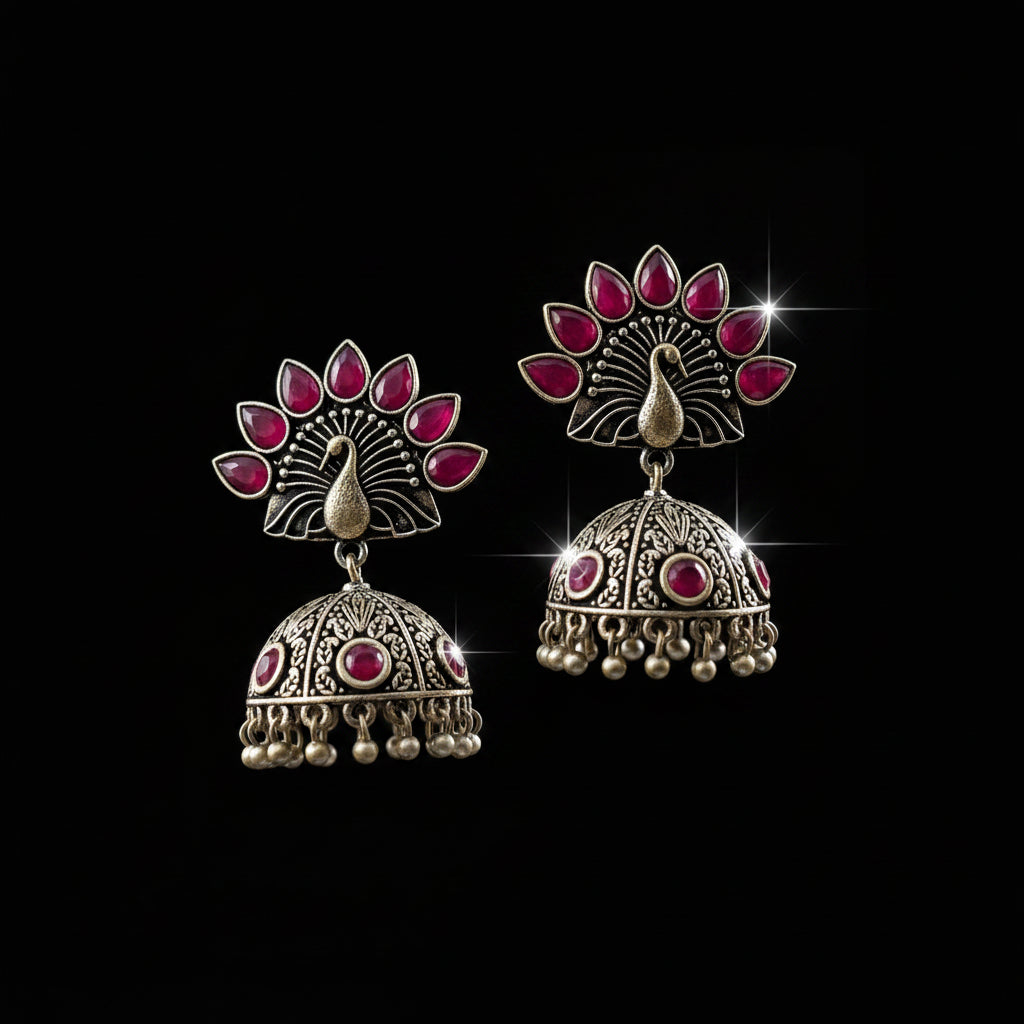 Ornate earrings with red stones on a gray stand, branded 'Saheli'.