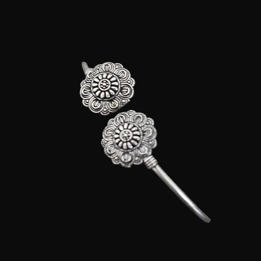 Silver floral earrings on a gray stand against a dark background